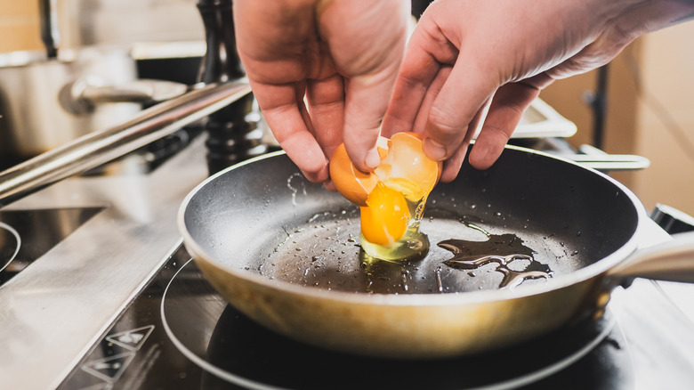 Person cooking an egg in a skillet