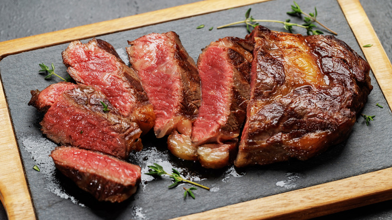 juicy sliced steak sitting on a board with fresh herbs