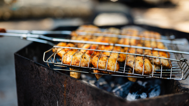 Mushrooms cook in a grill basket over a grill.