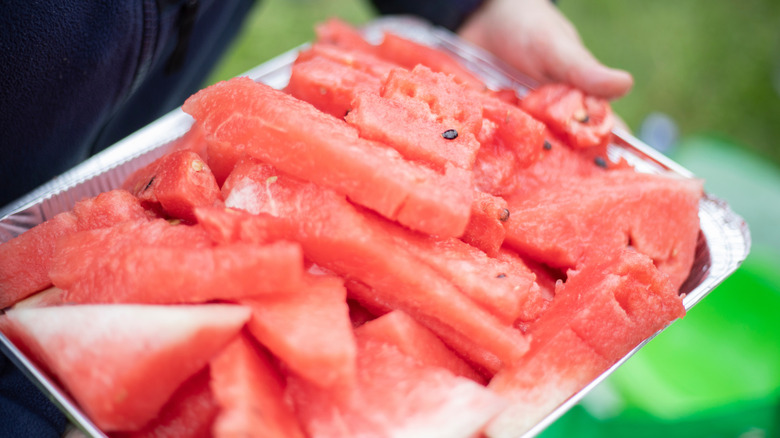 Person holding a tray of sliced watermelon