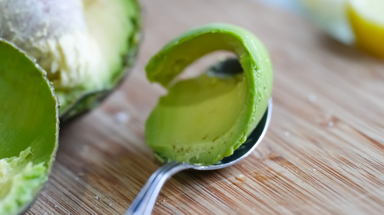 A spoon with avocado on a wooden board.