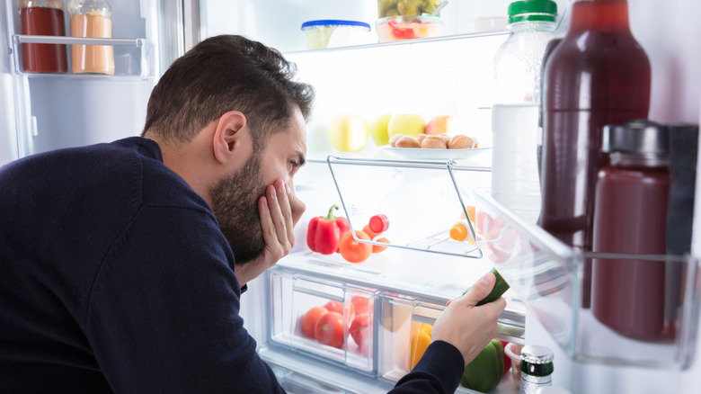 A man covering his nose in front of the fridge