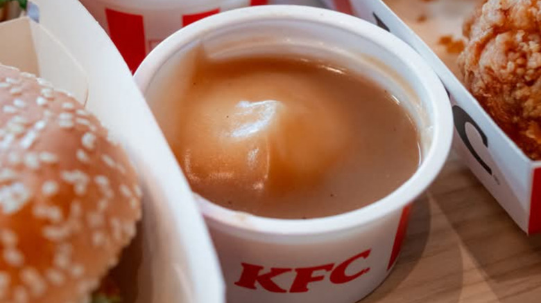 A tub of KFC potatoes and gravy, between a sandwich and a piece of fried chicken.