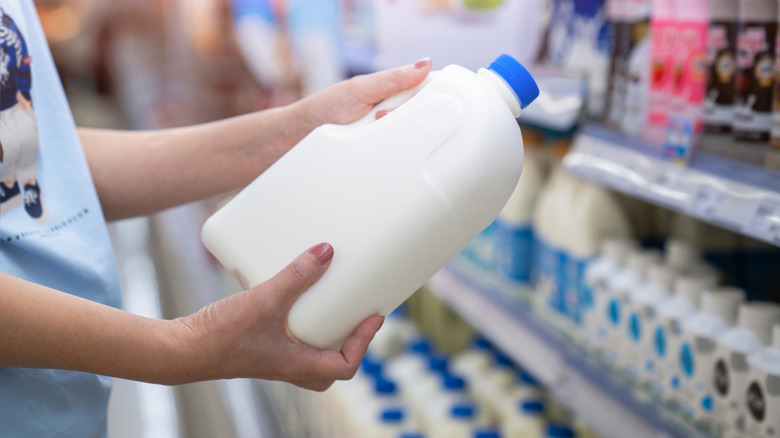 Hands holding a tub of unlabeled milk, with rows of other dairy options in the background