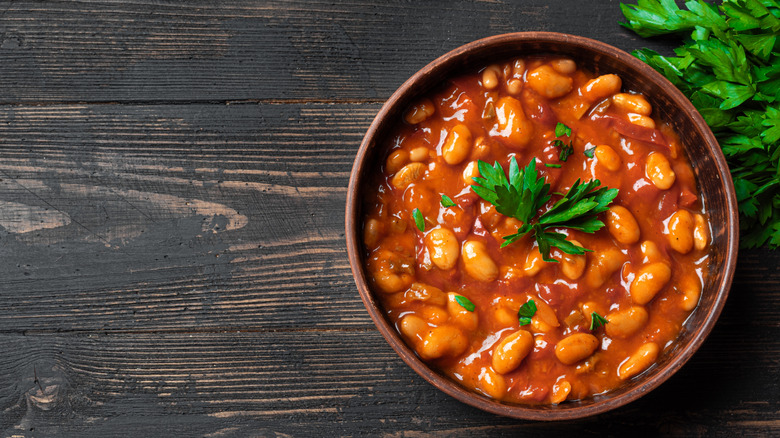 A bowl of baked beans on a wooden surface with fresh cilantro