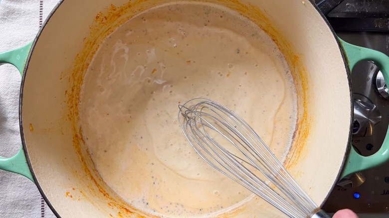 Whisking kimchi mac and cheese sauce in pot on stovetop