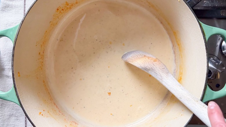 Stirring kimchi mac and cheese sauce with wooden spoon in pot on stovetop