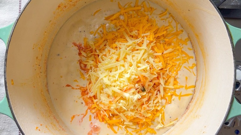 Shredded cheddar and smoked gouda on top of kimchi mac and cheese sauce in pot on stovetop