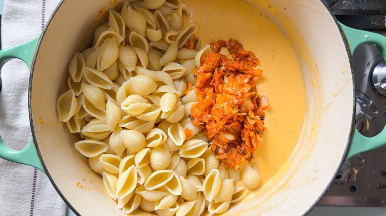 Cooked shell pasta and caramelized kimchi on top of cheese sauce in large pot on stovetop