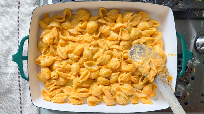 Layering kimchi mac and cheese into baking dish with wooden spoon