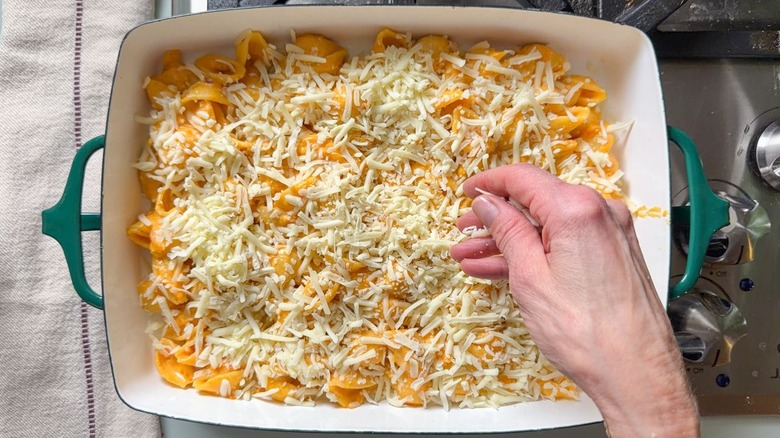 Sprinkling mozzarella cheese over kimchi mac and cheese in baking dish