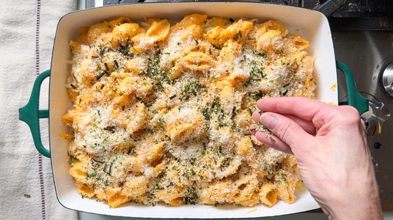 Sprinkling panko, parmesan, and furikake on kimchi mac and cheese in baking dish