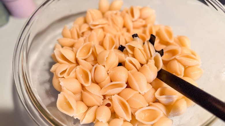 Tossing cooked pasta shells with olive oil in glass bowl