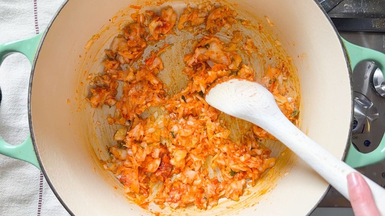 Stirring chopped kimchi with wooden spoon in large pot on stovetop