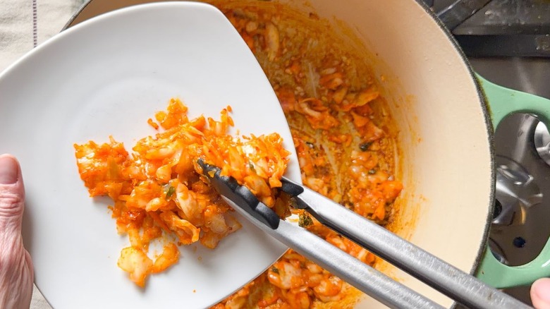 Using tongs to remove caramelized kimchi from pot to a plate
