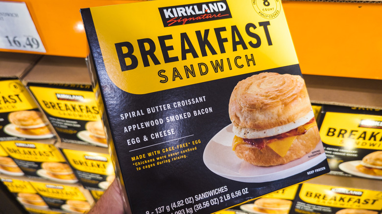 A person holds a box of Kirkland Signature breakfast sandwiches in front of an apparent display.