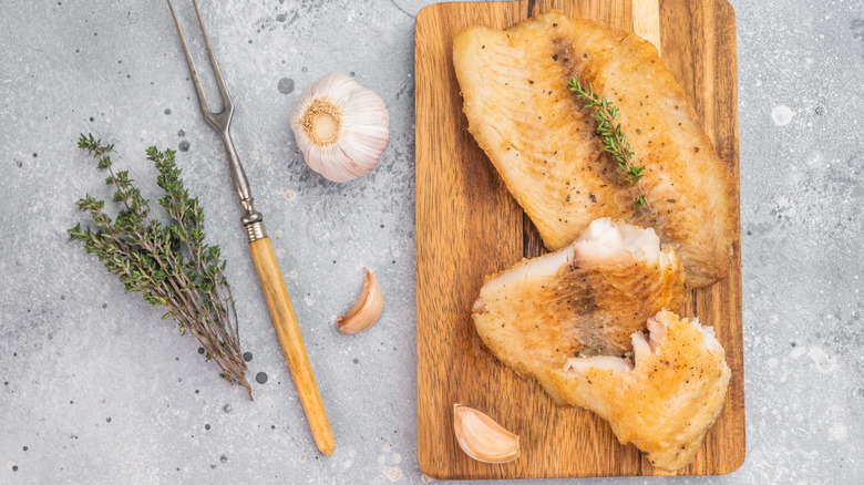 Cooked tilapia fillets on board with herbs and garlic on the side