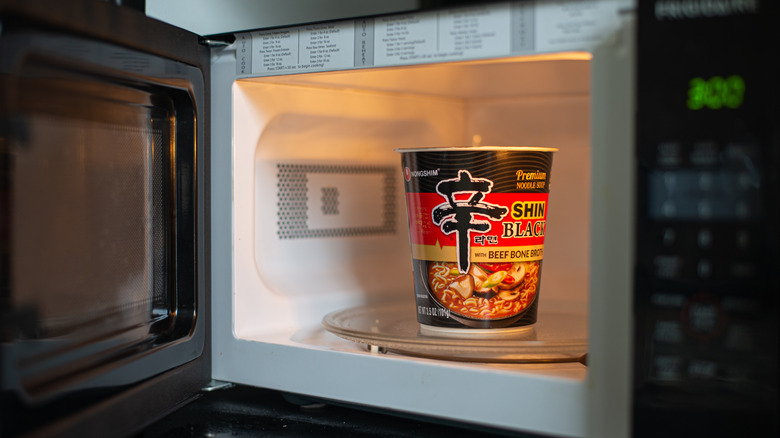 Person reheating microwave noodles in a microwave