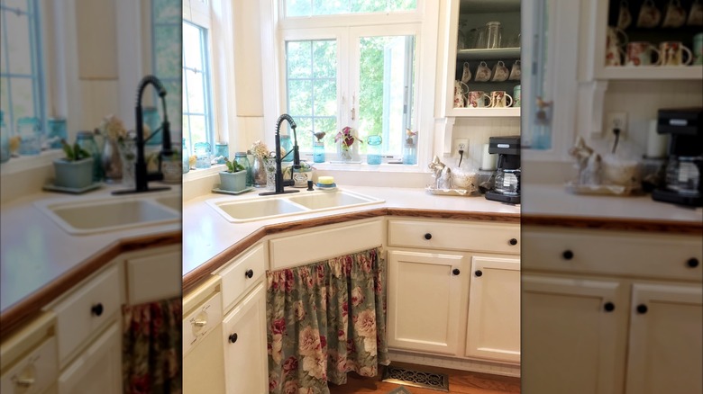 A minimalist white kitchen with wood accents and a floral sink curtain