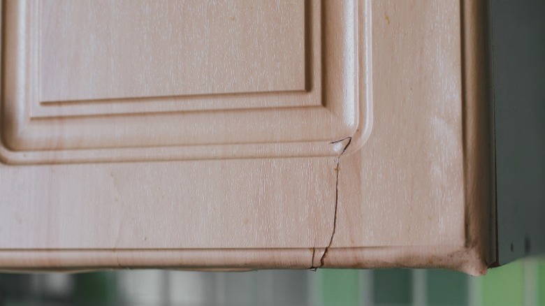 A cracking facade on a kitchen cabinet due to steam and heat damage.