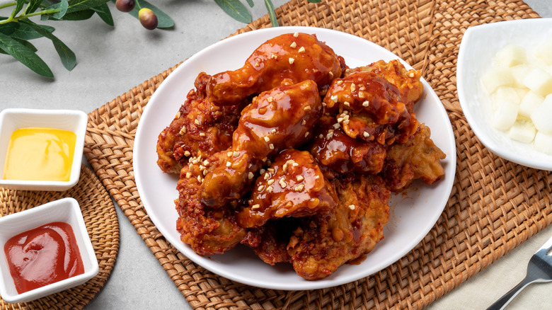 saucy Korean fried chicken on a white plate on a brown mat with more sauces around