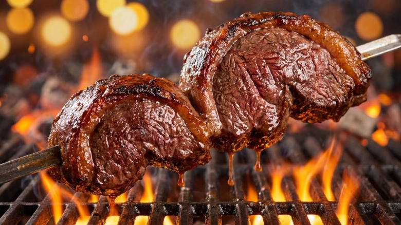 Two cuts of Brazilian Picanha beef cooking over flames on a skewer.