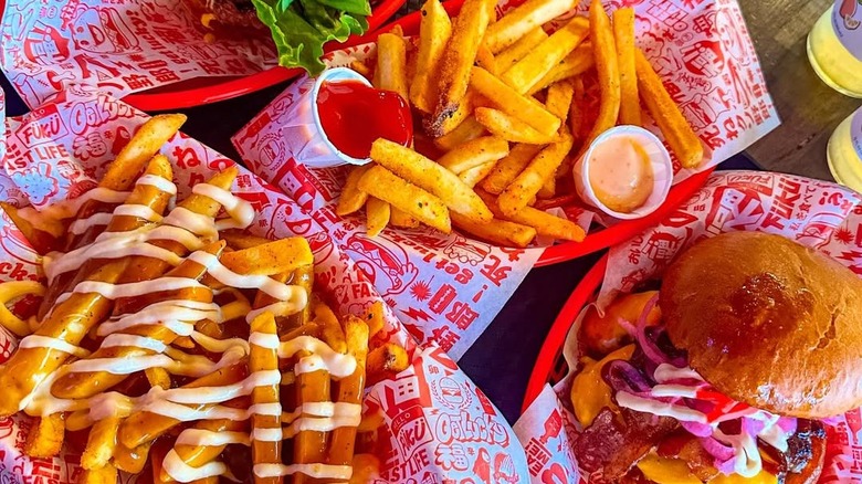A flat lay of several Fukuburger dishes, include two kinds of fries and a hearty burger.