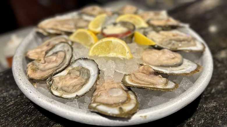 A platter of raw oysters on ice with lemon wedges from The Oyster Bar.