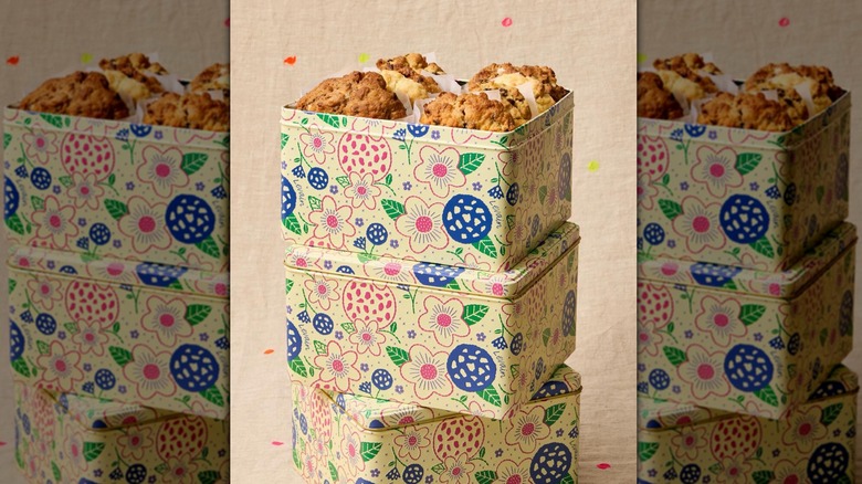 Three floral-decorated tins of Levain Bakery cookies stacked on top of one another