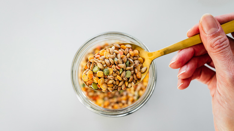 a person's hand scooping out a mix of legumes from a Mason jar