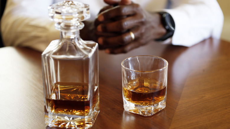 Whiskey decanter and glass with a person's arms in the background
