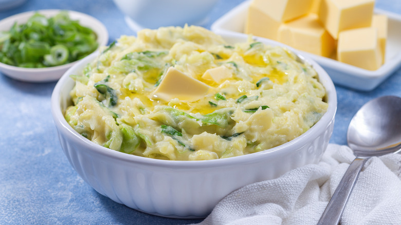 a big bowl of colcannon topped with melted butter alongside a serving spoon