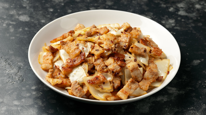 a plate of stir-fry cabbage with pork belly on a granite countertop