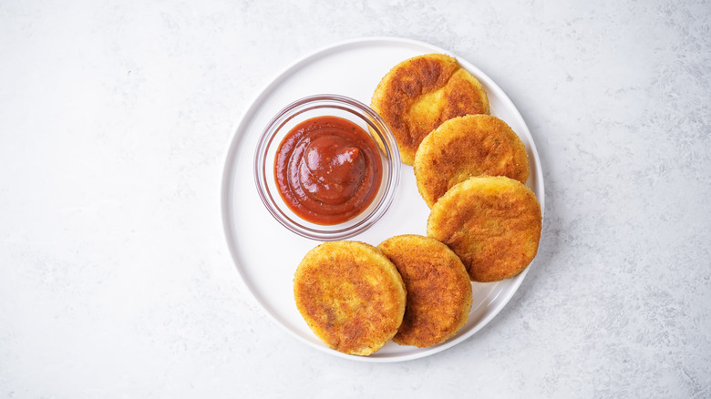 Fried potato patties on a white plate with a side of tomato dipping sauce