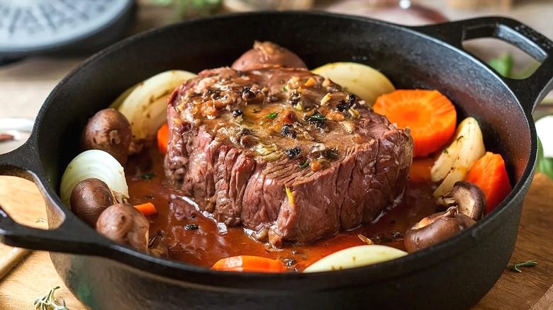 Cooked pot roast with chopped carrots, onions, and mushrooms in a cast-iron pot with handles.