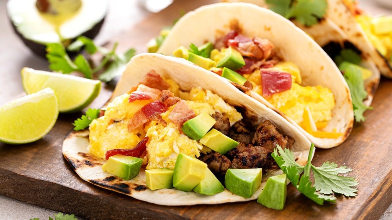 Two breakfast tacos with cooked meat, scrambled eggs, diced avocado, and fresh cilantro.