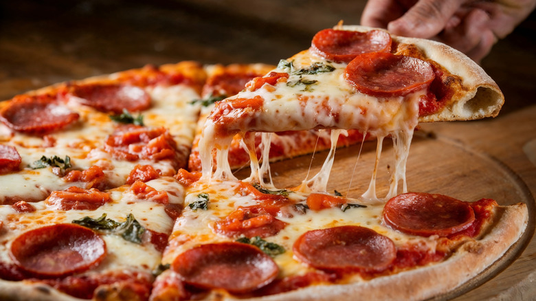 Pepperoni pizza slice being lifted from wooden board