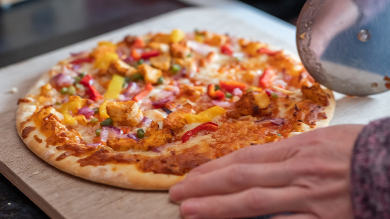 Close up of a thin crust sweet chilli chicken pizza on a wooden cutting board