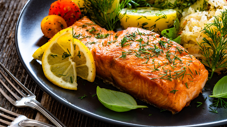 A cooked salmon filet on a plate with herbs and vegetables