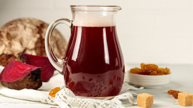 A jug of beetroot drink with beets and sugar lumps around it
