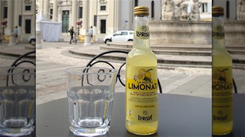 A bottle of carbonated limonata with a glass.