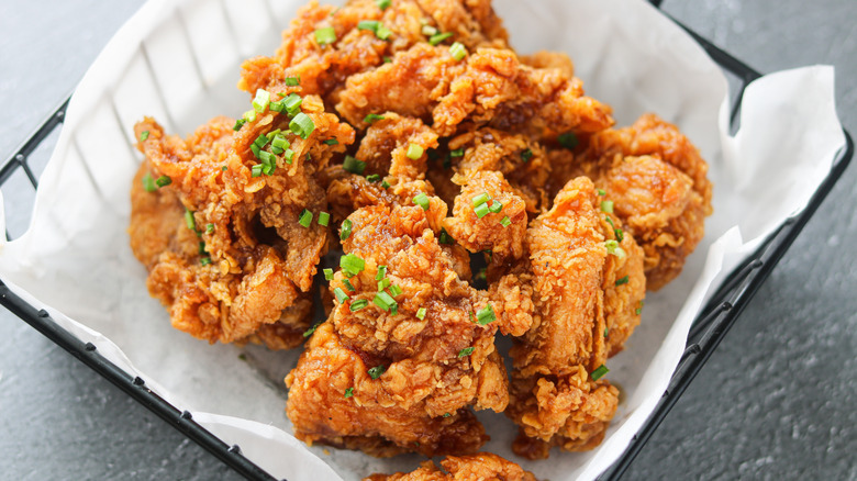 Closeup of Ganjang Chicken pieces (Korean soy-garlic fried chicken), garnished with chopped scallions. The chicken is served in a black wire serving basket lined with white paper.