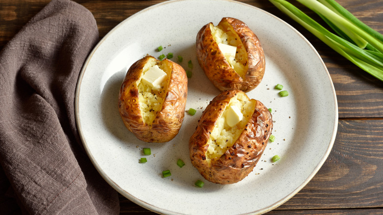 Three baked potatoes on a plate with butter