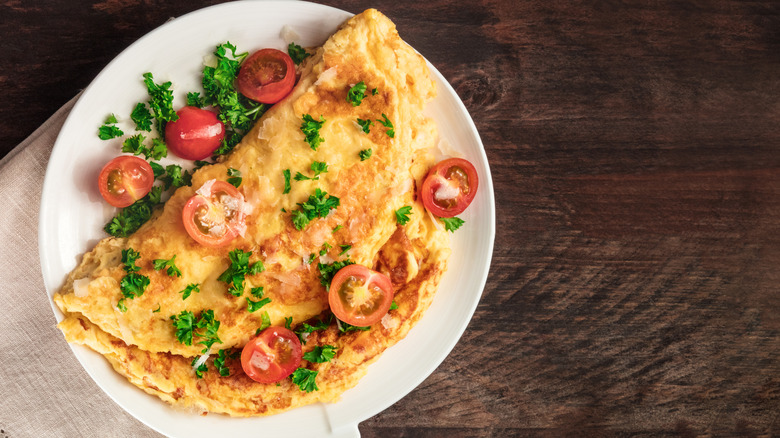 An omelet topped with sliced cherry tomatoes and fresh parsley