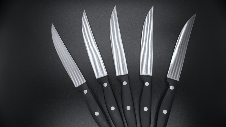Five steak knives spread out against a black background