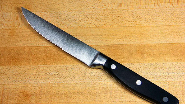 A serrated steak knife on a wooden cutting board.