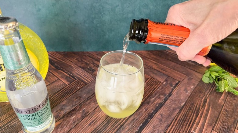 Pouring prosecco over limoncello and ice in a balloon glass