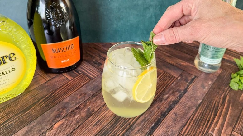 Adding a mint sprig and lemon wheel to a limoncello Amalfi spritz