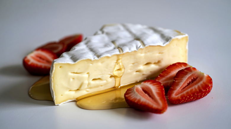 A wedge of brie with honey drizzled on it and sliced strawberries