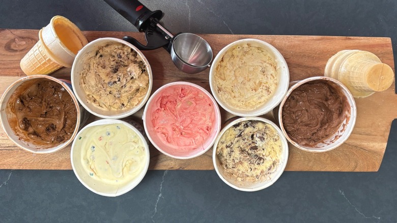 Aerial view of 7 Little Debbie ice cream pints with scooper and cones on cutting board and gray counter